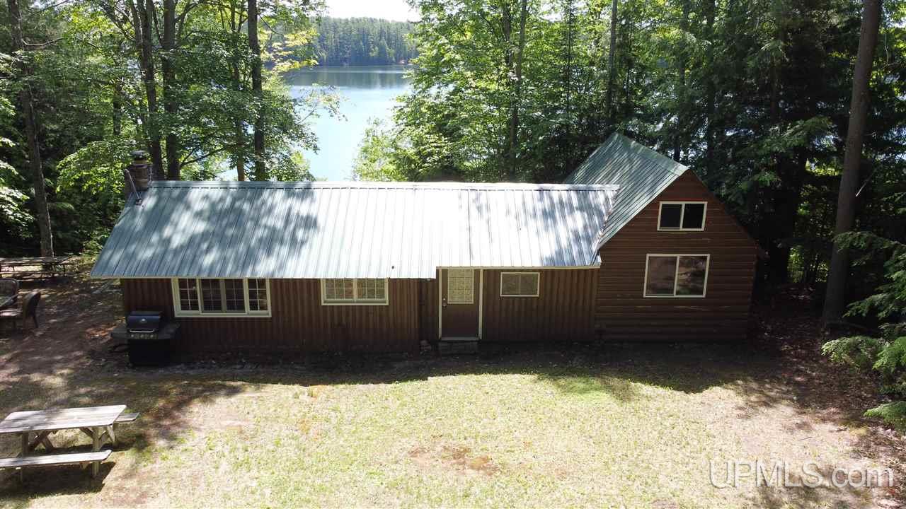 How about this cottage & piece of land that’s on Straights Lake? This is a very sought after and popular lake with great fishing & boating relaxation. The area is adored by many being the northernmost attachment to the wonderful “Chain of Lakes”.  This 2 bedroom / 1 bath log built construction also comes with an overlooking dining/sun room and has a stunning view of the lake. The kitchen/dining/living room area has the more rustic look and the bedroom and bath area is newer tongue and groove cedar and recently upgraded. The master bedroom faces the lake and exhibits potential for a walk-out deck that could either connect to the dining room or wrap around the entire front of the building. Heading down the bottom of the graded landscape to a beautiful sandy swimming beach presents a gorgeous view of the lake whether it is at the bottom or on the platform slightly elevated above. Many varieties of trees cover the property as you enter and look to the lakeside. Set yourself in a great environment with many beautiful connected lakes and the tranquility these lovely inland lakes provide.